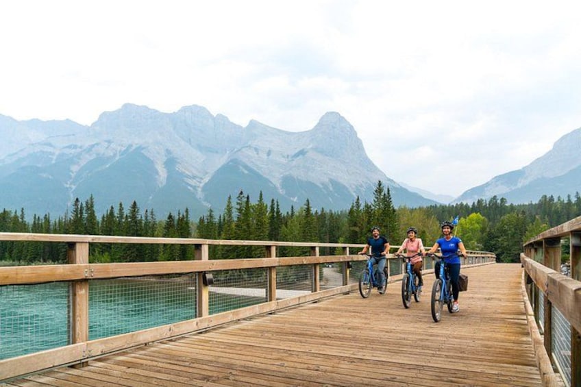 A wooden bridge with cyclists, a lake, and mountains in the background. 5