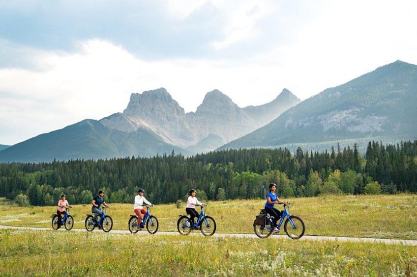 A group of cyclists on a trail with mountains in the background. 3