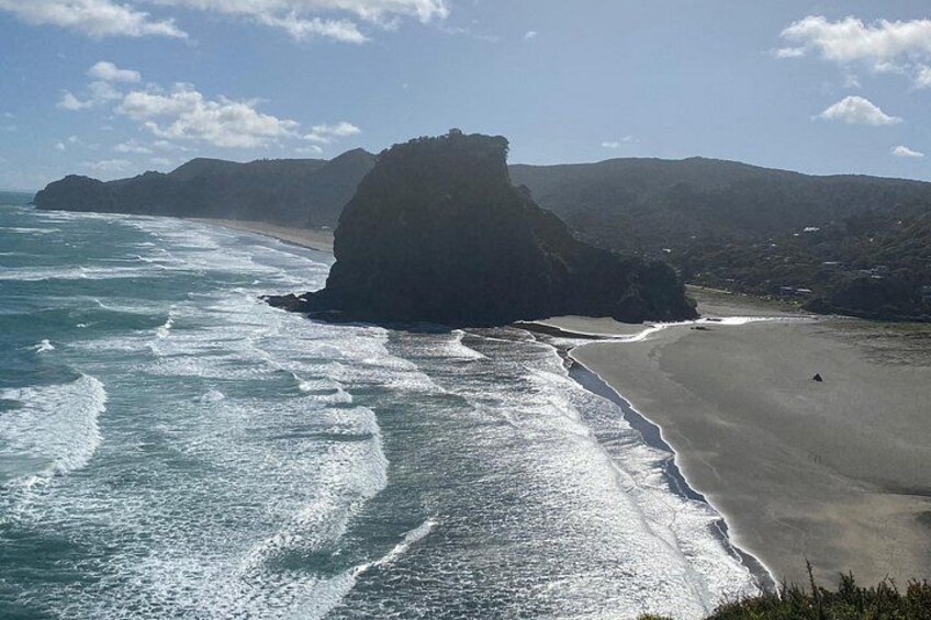 A coastal landscape with a large rock formation, a sandy beach, and ocean waves. 1