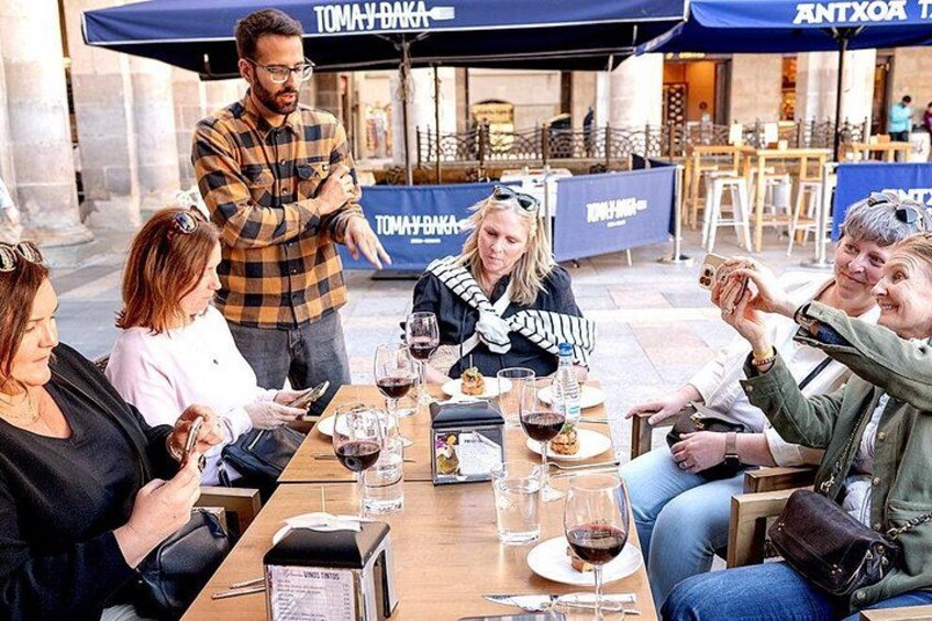 A group of people seated at an outdoor table with wine glasses and a menu. 4