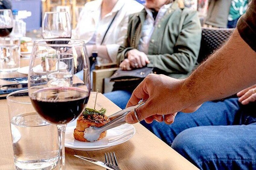 A dining table with a glass of red wine, a plate with food, and a person holding a fork. 5