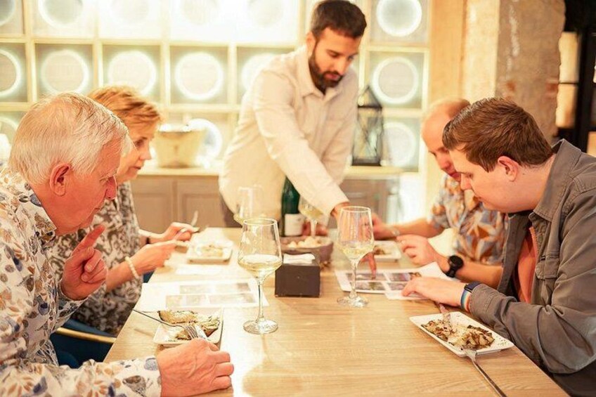 A group of people dining at a table with plates of food and wine glasses. 1