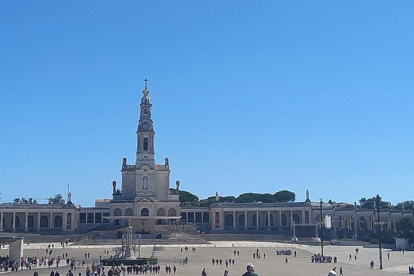 Ein großes historisches Gebäude mit einem markanten Turm, einem weitläufigen Platz und blauem Himmel. 1