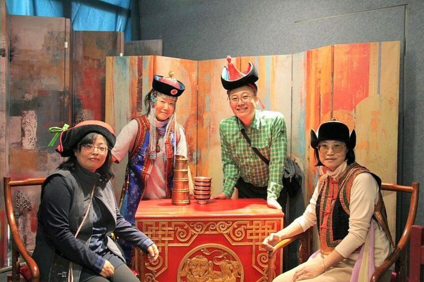Een groep mensen in traditionele kostuums zitten aan tafel met een rode tafelkleed en een decoratieve doos. 4