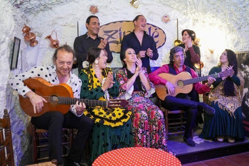 Un grupo de personas actuando en un escenario con instrumentos musicales, en una sala con decoración rústica. 1