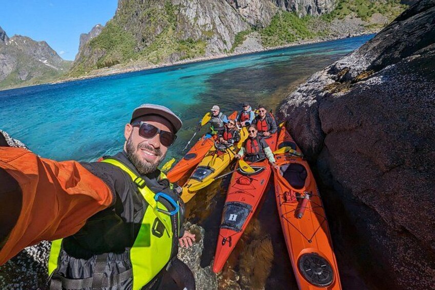 A group of people in kayaks near a rocky shore with clear blue water and mountains in the background. 4