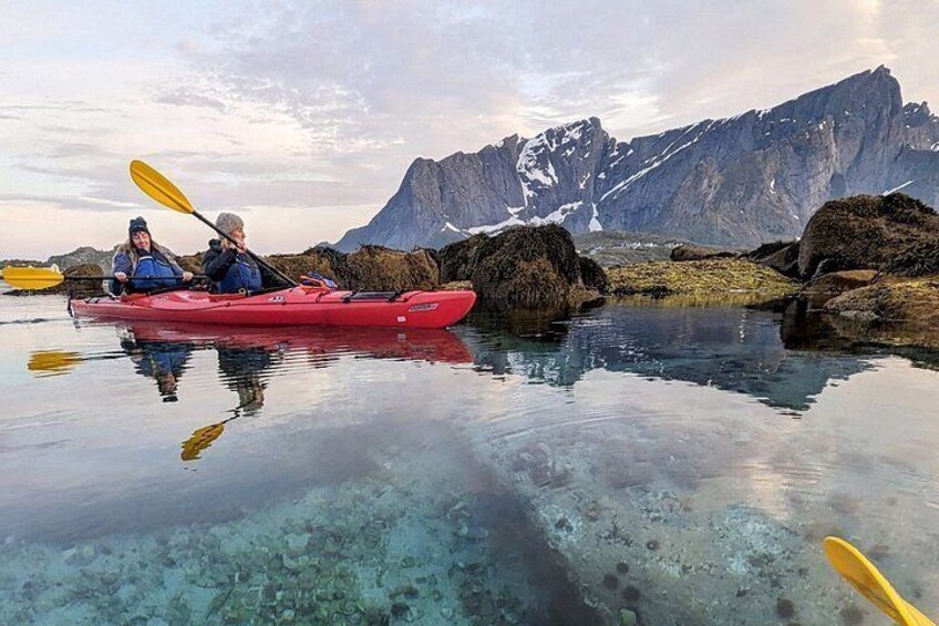 Two people kayaking on a calm lake with clear water, surrounded by rocky terrain and mountains in the background. 2
