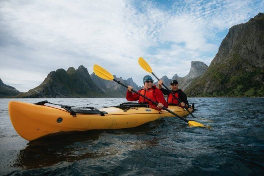 Two people kayaking on a calm body of water with mountainous terrain in the background. 1