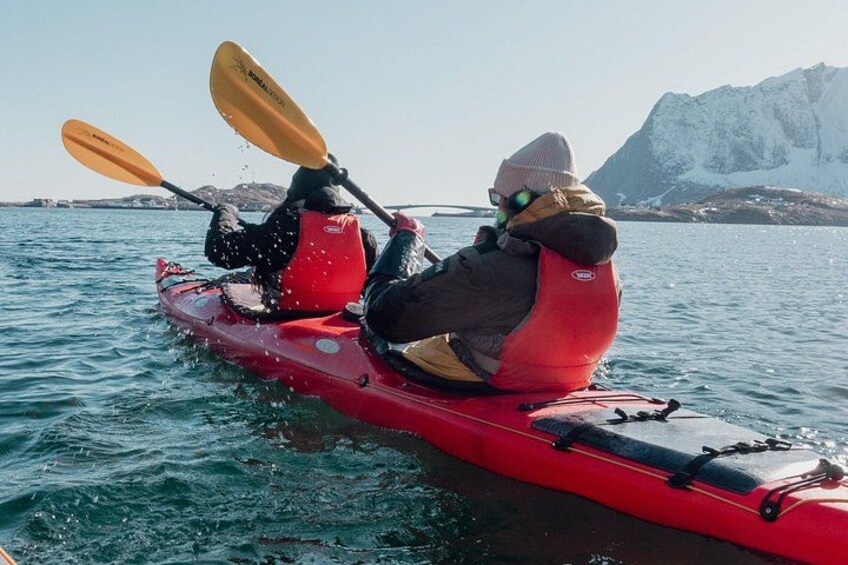 Two people kayaking on a calm body of water with a mountainous landscape in the background. 3