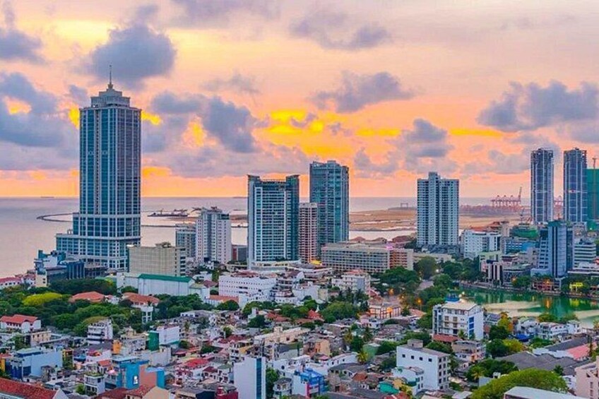 A cityscape with high-rise buildings, a body of water, and a sunset sky. 1