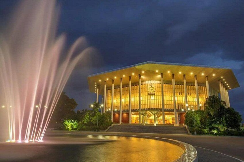 A grand building with a large fountain in front, illuminated by lights. 3