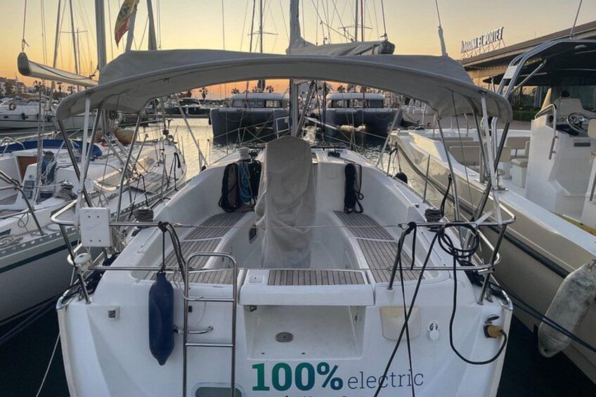 A sailboat docked at a marina with other boats, a clear sky, and a bridge in the background. 2