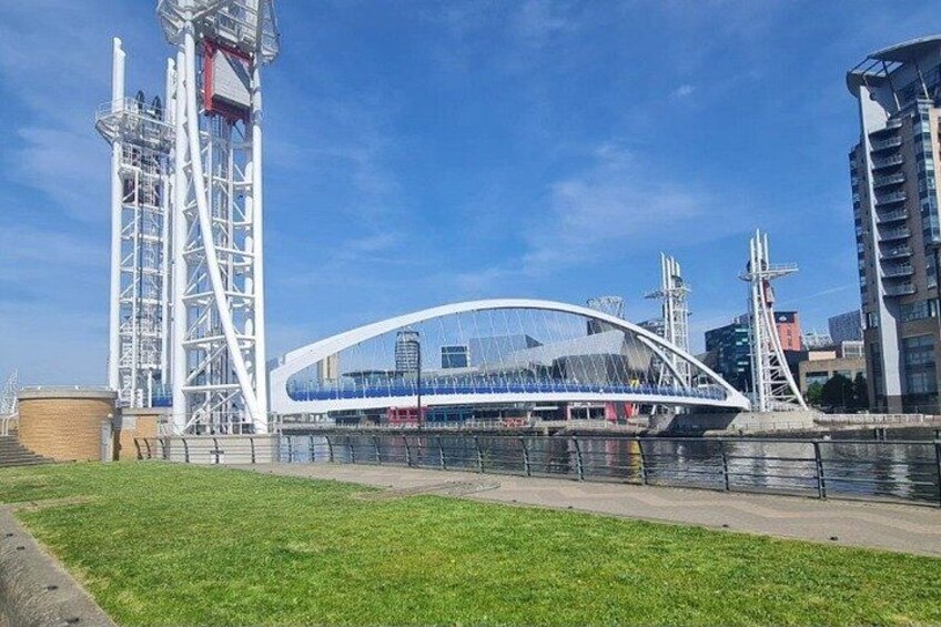 Un pont moderne avec une arche blanche et un intérieur bleu, une rivière et un paysage urbain avec des bâtiments et une grue. 3