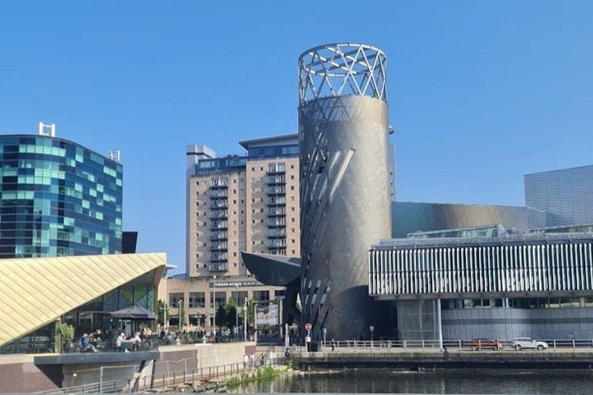 Un paysage urbain moderne caractérisé par un imposant bâtiment cylindrique, un gratte-ciel en verre et une zone riveraine dotée d’une promenade piétonne. 2