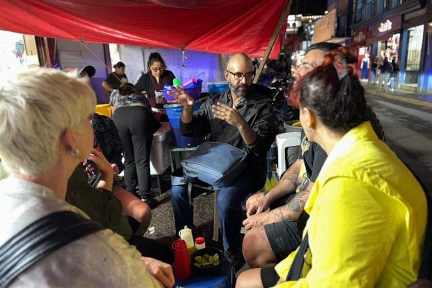 Un grupo de personas sentadas bajo un toldo rojo, conversando. 2