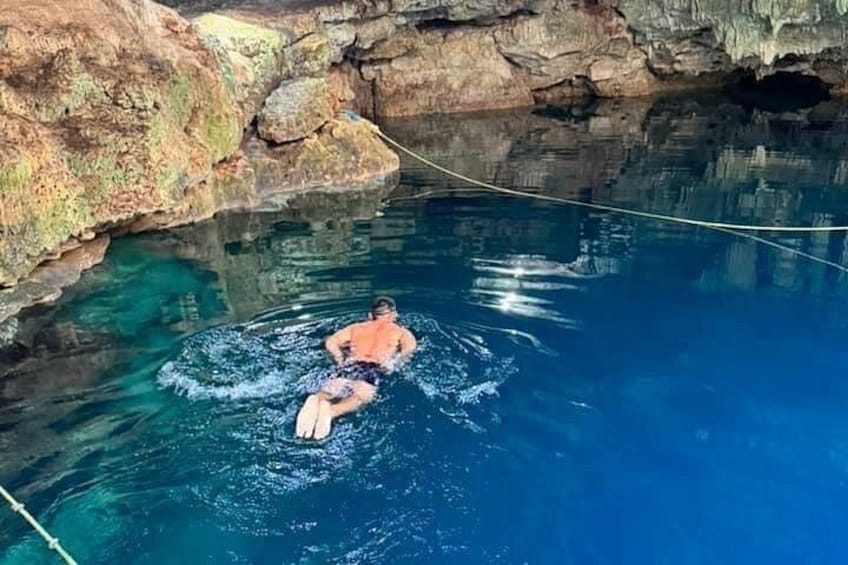 A person swimming in a clear blue pool with rocky walls. 1
