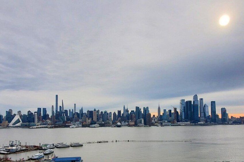 A city skyline with numerous high-rise buildings, a body of water in the foreground, and a clear sky. 2
