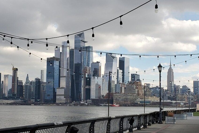 A city skyline with modern skyscrapers, a river, and a bridge with string lights. 3