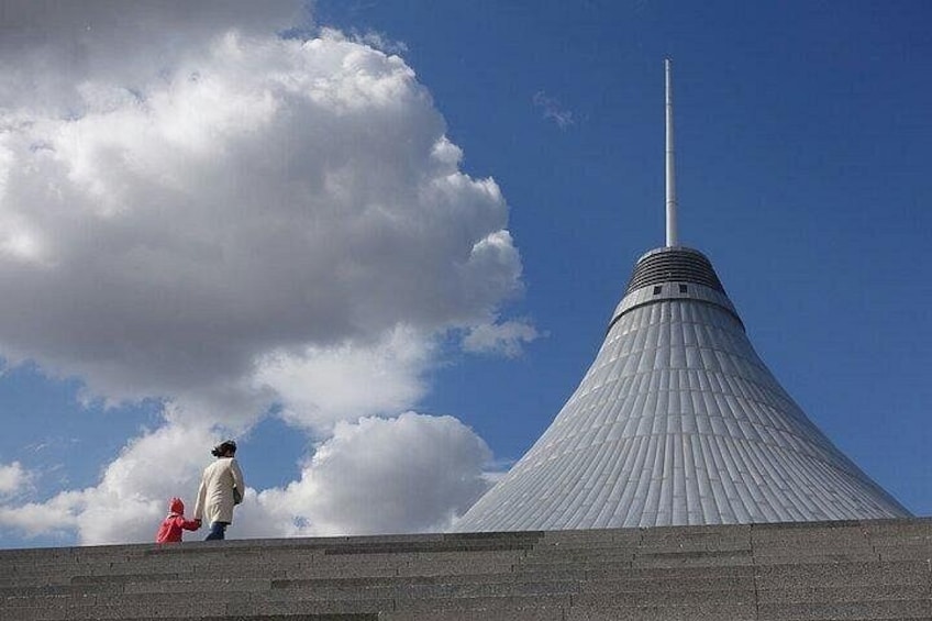A large, conical structure with a tall spire, a person in a red jacket, and a partly cloudy sky. 4