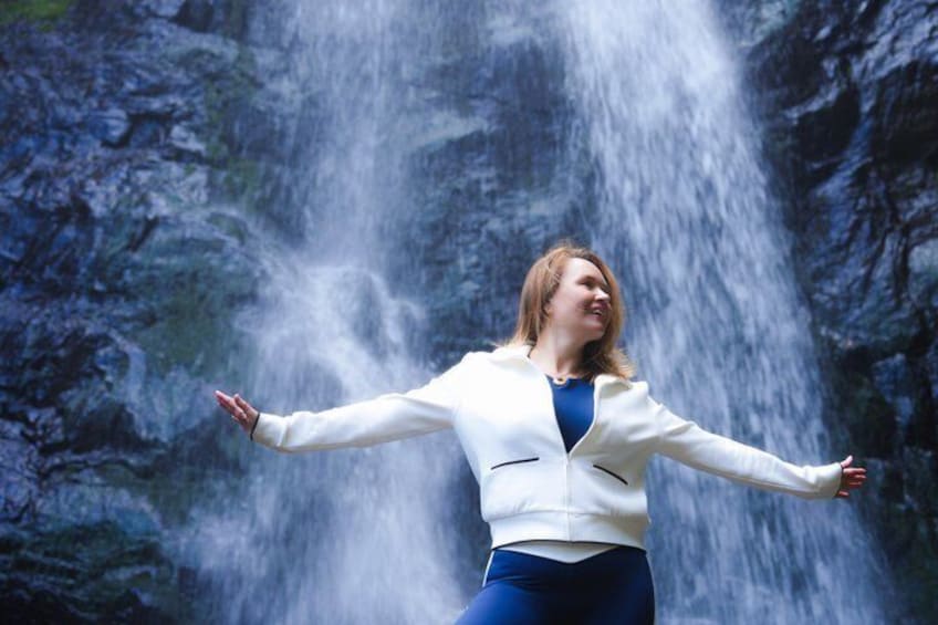 A person standing with arms outstretched in front of a waterfall. 2