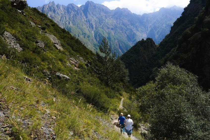 A hiking trail with hikers, surrounded by mountainous terrain and dense greenery. 3