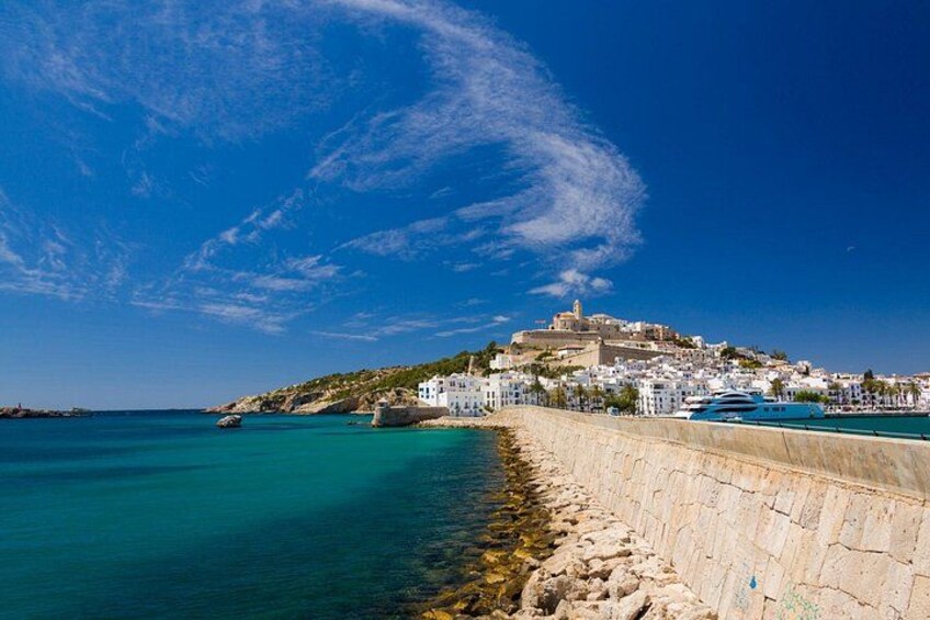 A coastal town with a stone wall, calm sea, and a hilltop building. 5