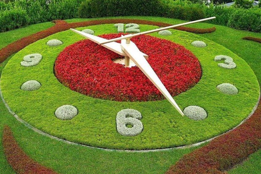 A garden clock with red flowers and green grass. 3