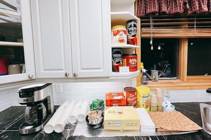 A kitchen counter with various food items, a coffee maker, and a window with curtains. 3