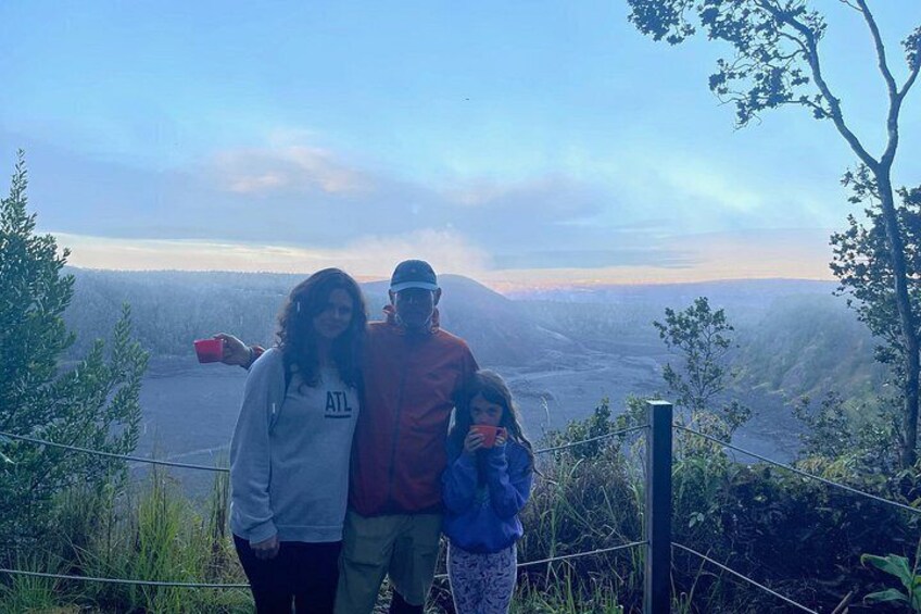 Three people standing on a hill with a scenic view of a valley and mountains in the background. 3