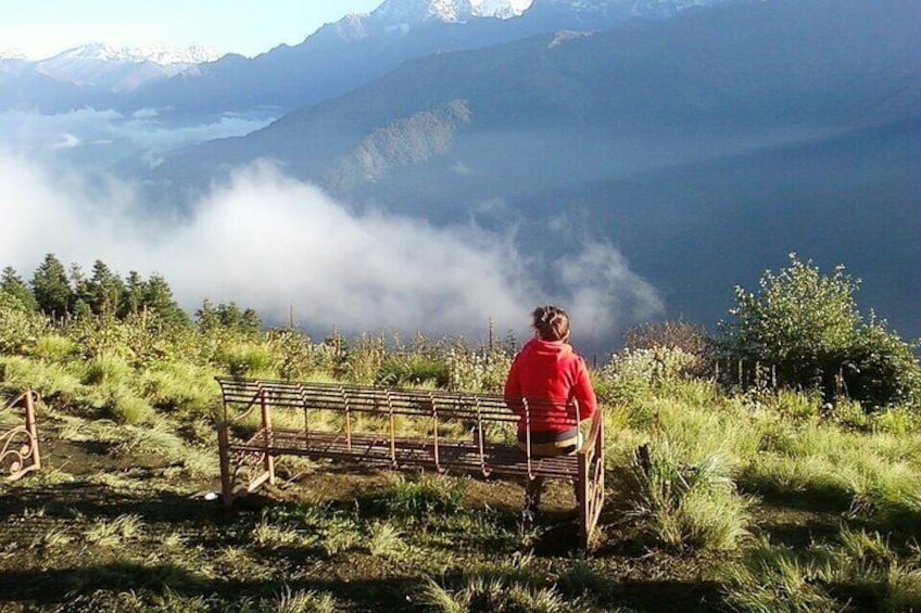 A person sitting on a bench overlooking a mountainous landscape with clouds below. 4