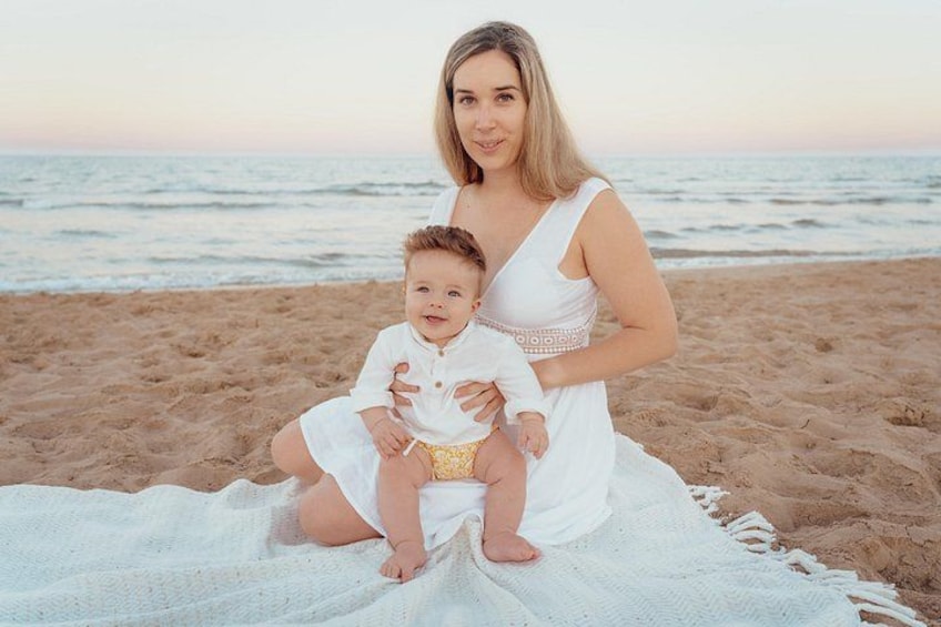 A woman and a child sitting on a blanket on a beach with the ocean in the background. 1