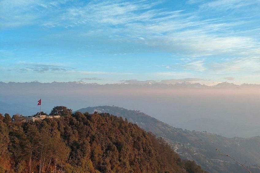 A mountainous landscape with a flag on a hill, dense forest, and distant mountain ranges. 5