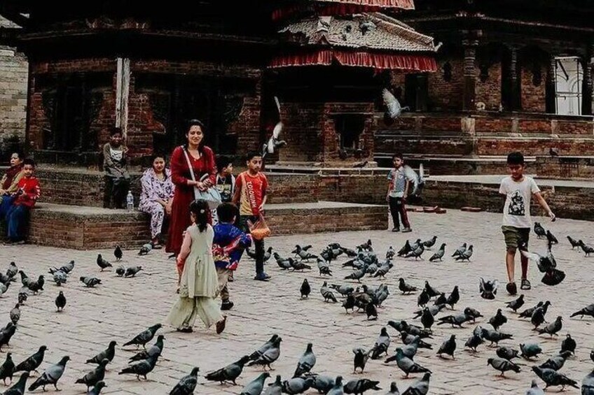 A group of people feeding pigeons in a courtyard with a traditional building in the background. 4