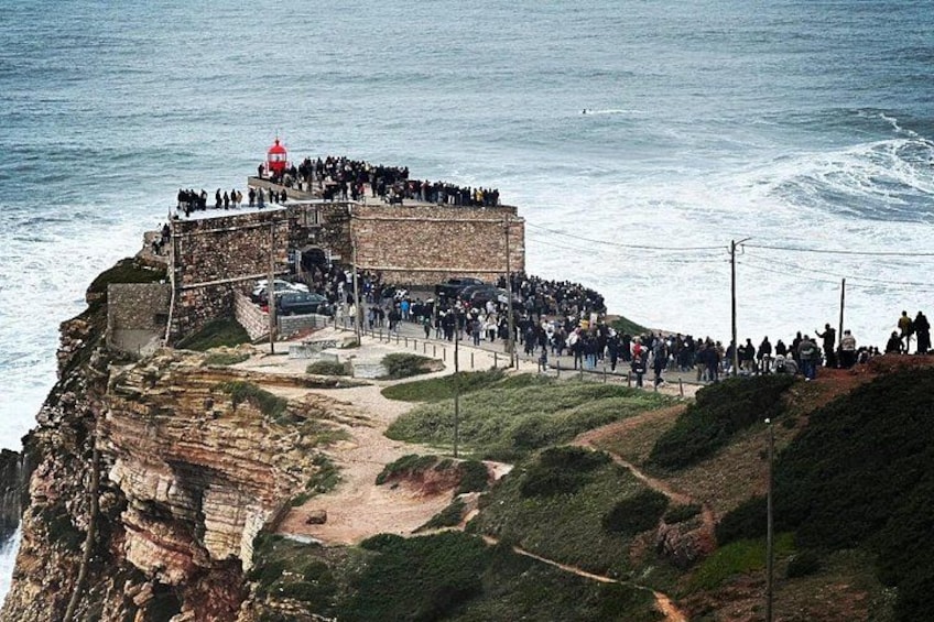 A coastal fortification with a crowd of people gathered on its walls. 1