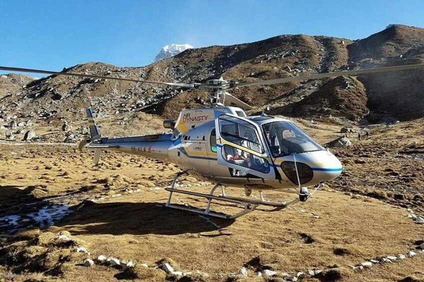 A helicopter with 'CRYSTAL' written on it, parked on rocky terrain with mountains in the background. 1