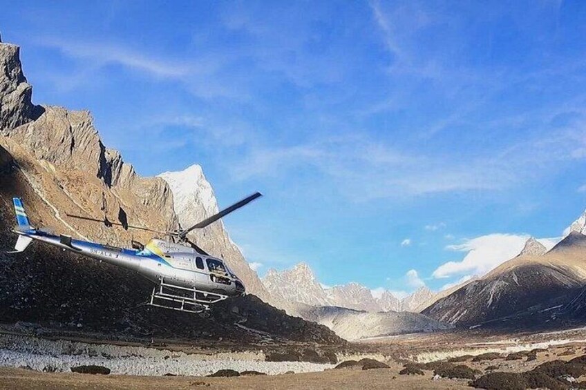 A helicopter parked on a mountain slope with snow-covered peaks in the background. 3