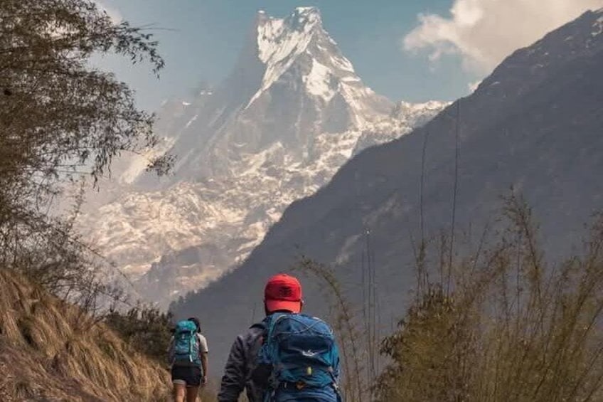 Dos excursionistas caminando por un sendero de montaña con un pico nevado al fondo. 1