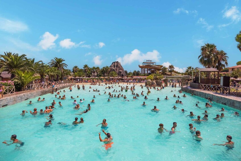 A large outdoor swimming pool with people swimming, surrounded by palm trees and a mountain in the background. 3