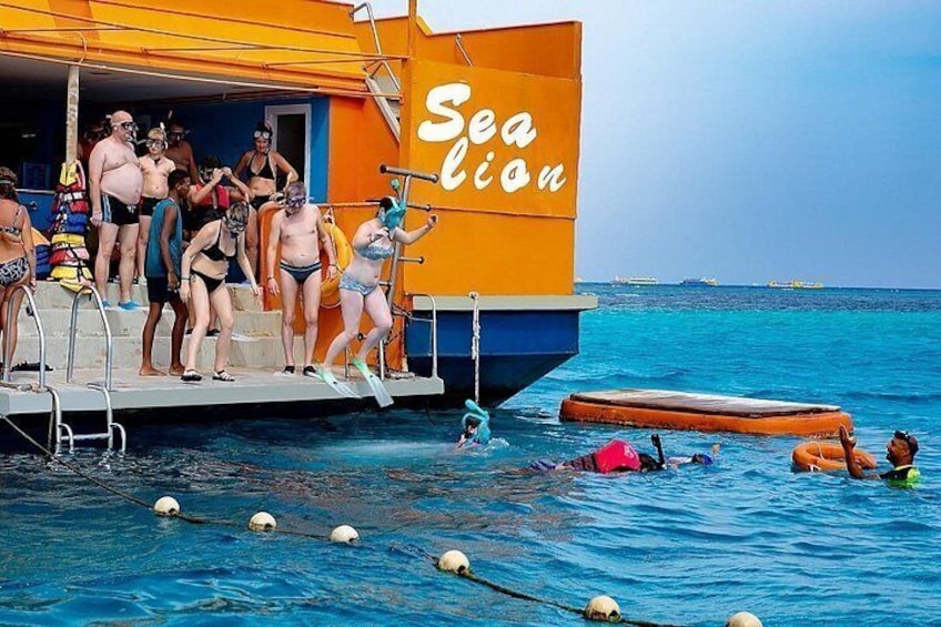 A swimming pool with people preparing to enter the water, a lifeguard tower, and a boat named 'Sea Lion' in the background. 5