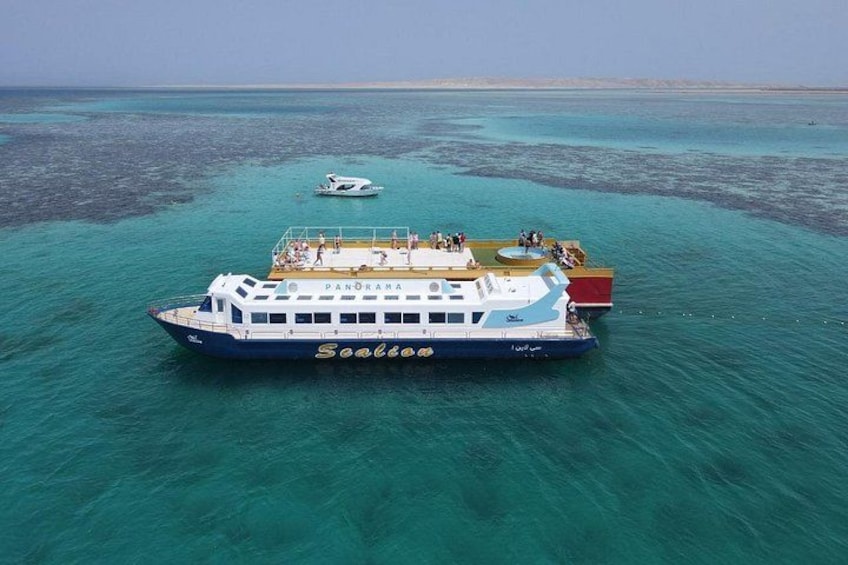 A large boat named 'Panorama' with 'Seaboo' written on its side, floating on turquoise water with a clear sky above. 1