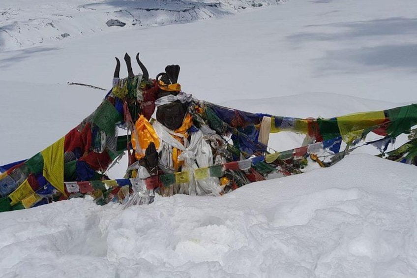 A snow-covered landscape with colorful prayer flags and a yak statue. 3