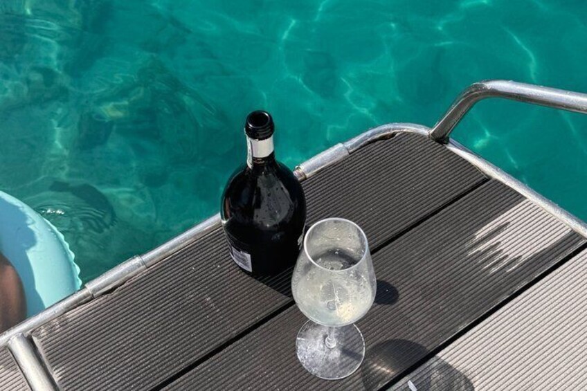 A bottle of wine and a glass on a metal deck by a clear blue pool. 4