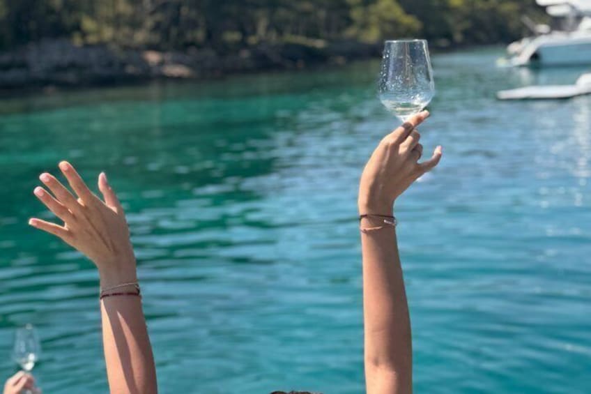 A person holding a glass of white wine with a clear blue body of water and boats in the background. 5