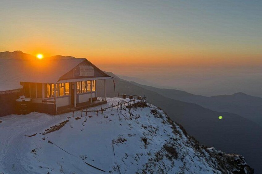 Cima innevata di una montagna con un piccolo edificio sulla vetta durante il tramonto. 1