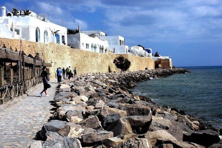 A coastal walkway with white buildings, a stone wall, and the sea. 1