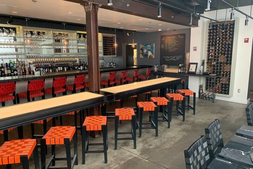 A bar with long tables, red chairs, and a wine rack. 1