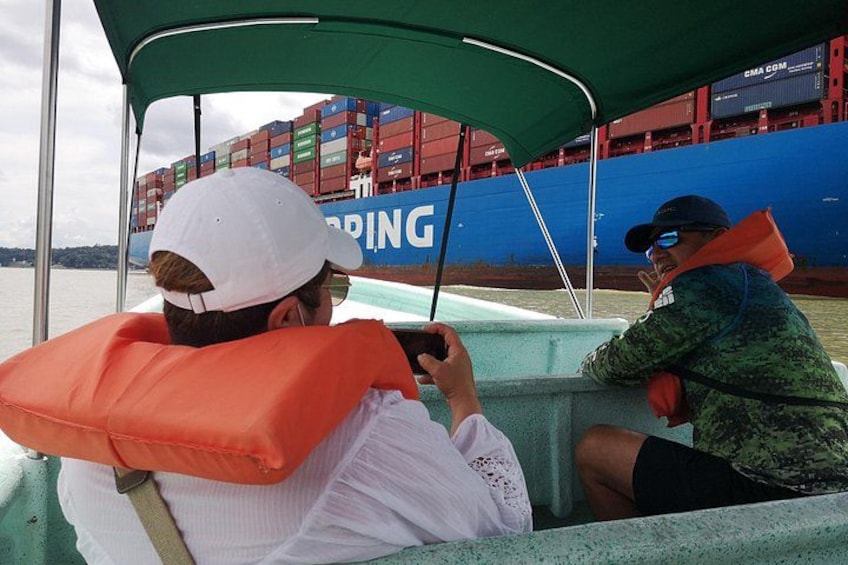 Two people on a boat with a large cargo ship in the background. 2