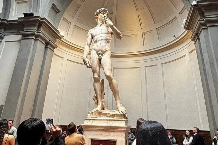A marble statue of a standing man in a classical pose, surrounded by onlookers. 1