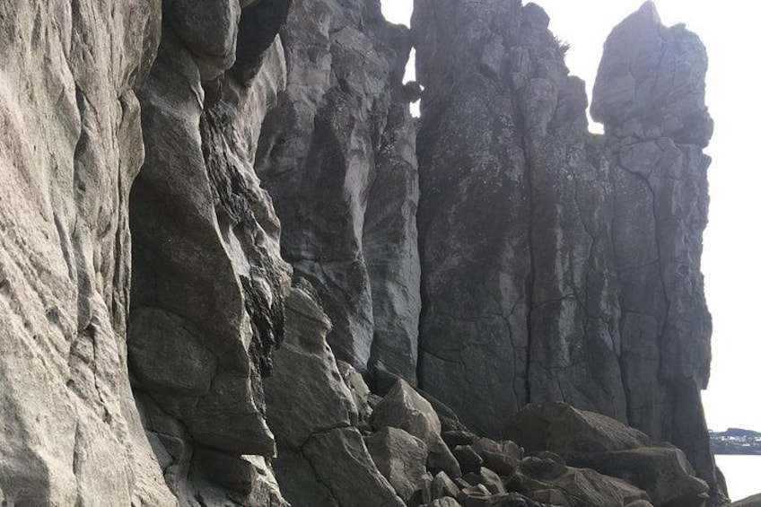 En karg klippvägg med tydliga spår av erosion och en kustlinje i fjärran. 2