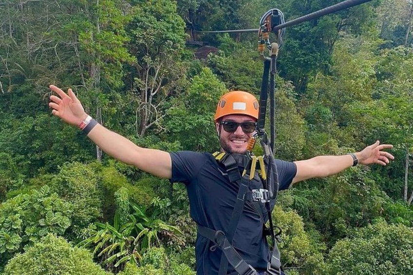 A person wearing a helmet and harness, standing with arms outstretched in a forested area. 4